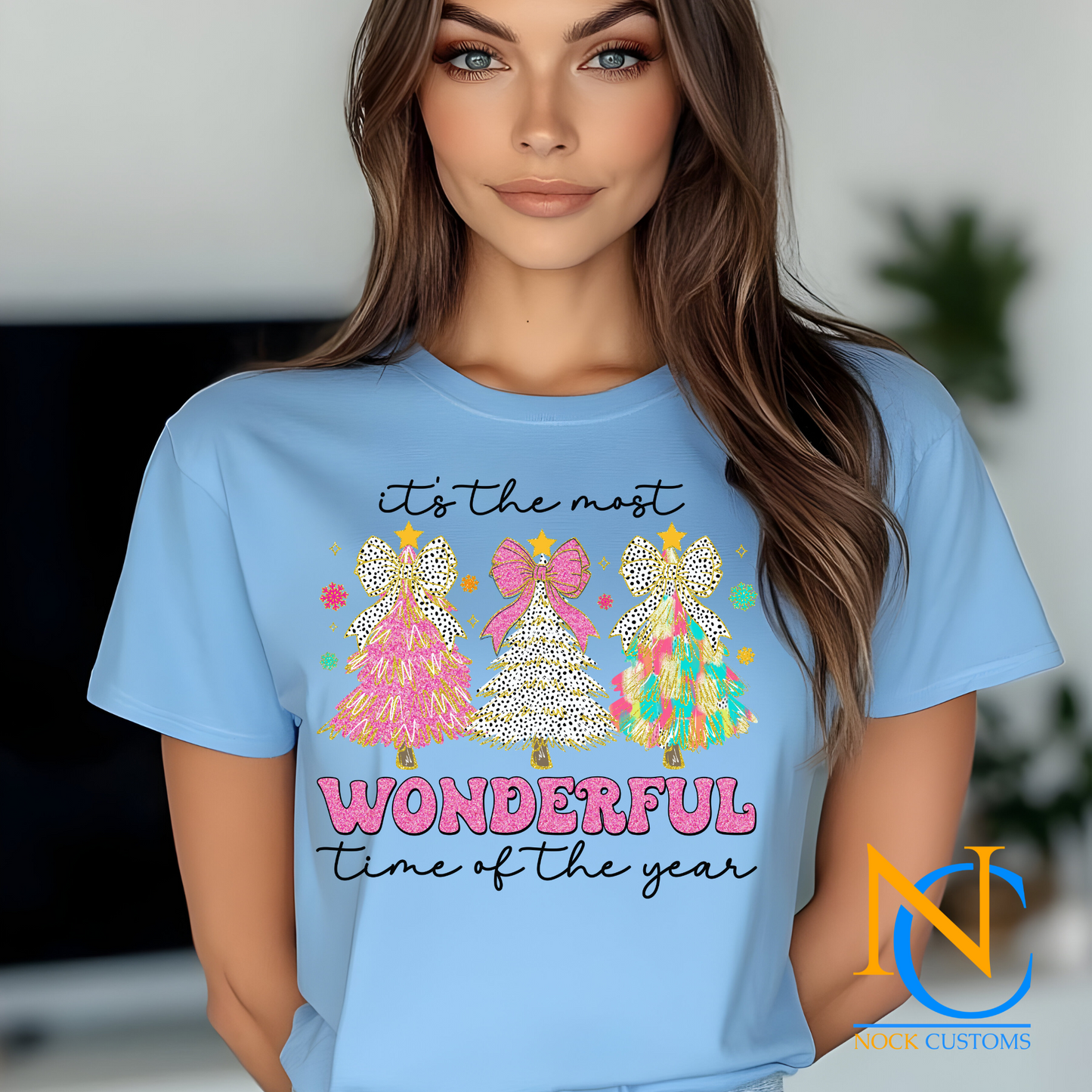 Bright and festive Christmas tree trio design with pink, polka dots, and multicolored trees reading 'It's the most wonderful time of the year' on various t-shirt colors.