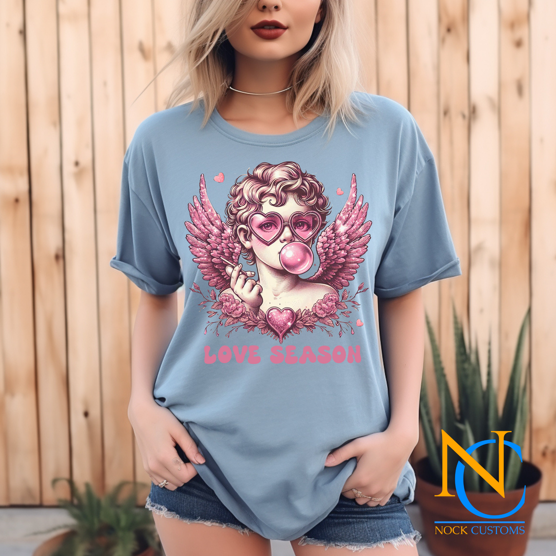 A whimsical design featuring a pink-toned angel wearing heart-shaped sunglasses, blowing bubble gum, surrounded by glittery wings, flowers, and a sparkling heart. The text 'Love Season' completes this romantic and playful design, perfect for direct-to-film (DTF) transfers.