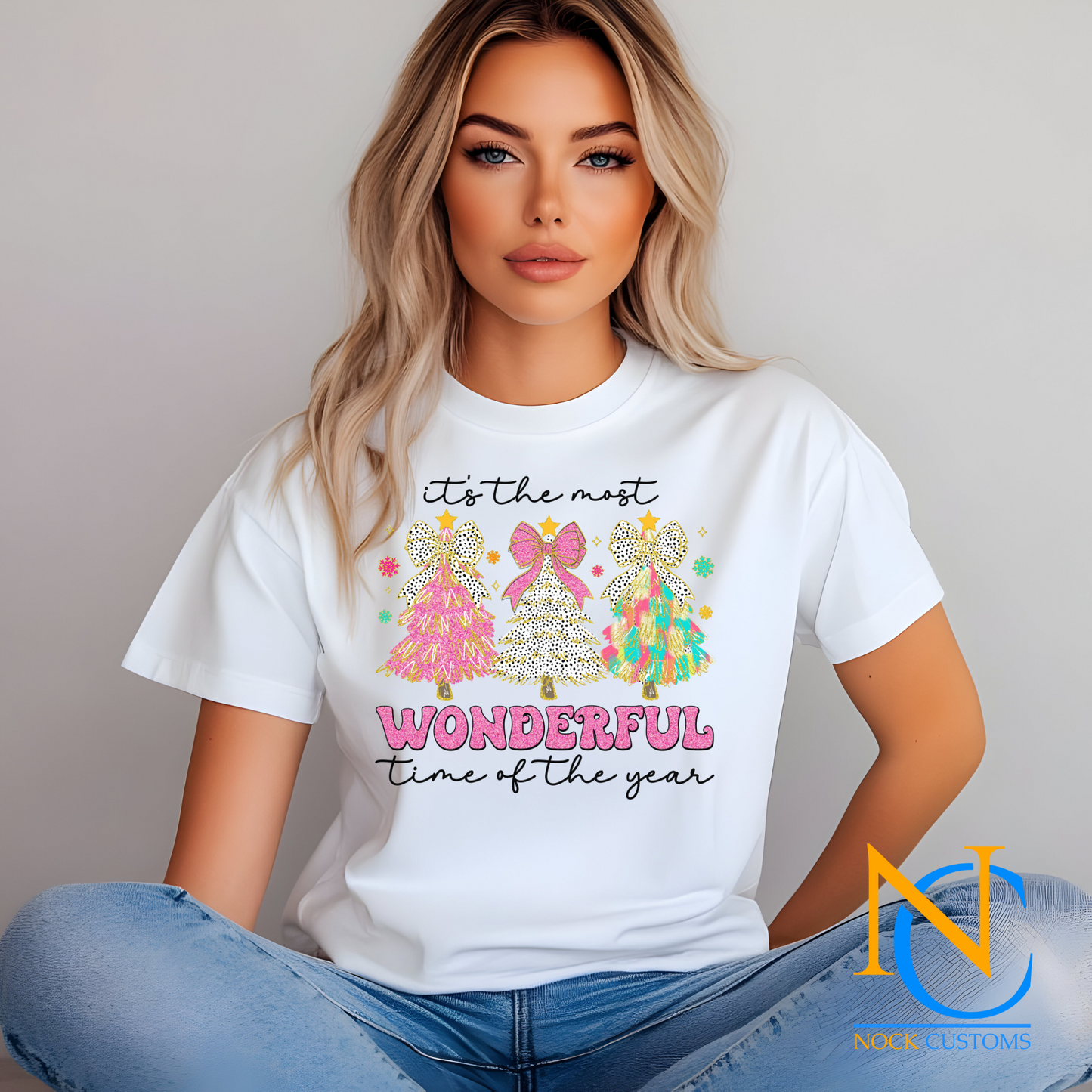 Bright and festive Christmas tree trio design with pink, polka dots, and multicolored trees reading 'It's the most wonderful time of the year' on various t-shirt colors.